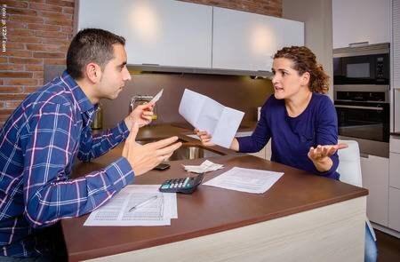 Una mujer y un hombre discutiendo por el dinero con papeles y calculadora encima de la mesa 