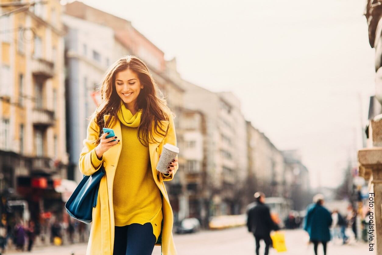 Mujer caminando por la calle con un celular en la mano