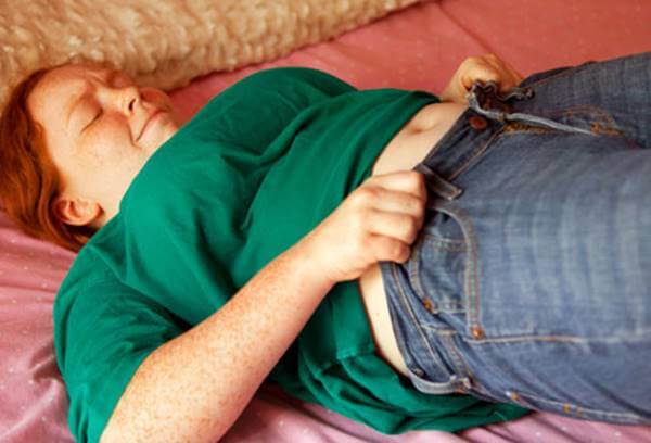 Foto de una adolescente con soobrepeso tratando de ajustarse el pantalón